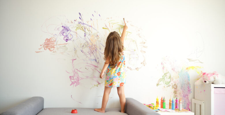 Dziecko rysuje po ścianie pomalowanej jasną farbą do wnętrz