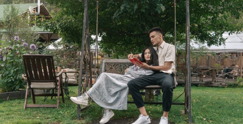 Para siedzi w ogrodzie na huśtawce i czyta książkę